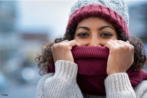 Woman in a knit hat and sweater covering her face with her scarf