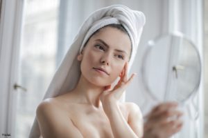 Woman with her hair in a towel looking at her skin in a mirror